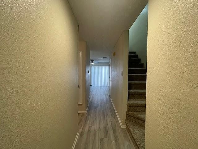 Hall with a textured wall, wood finished floors, and stairs