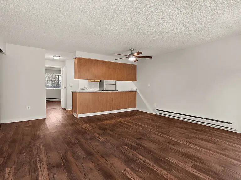 Spacious open-plan living area with rich wooden floors, a modern kitchen featuring sleek cabinetry, and a ceiling fan for comfort. Spacious open-plan living area with rich wooden floors, a modern kitchen featuring sleek cabinetry, and a ceiling fan for co