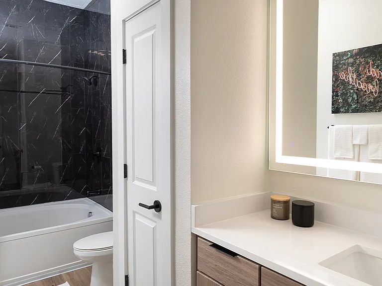 Apartment bathroom with wood-style flooring and LED vanity mirror.