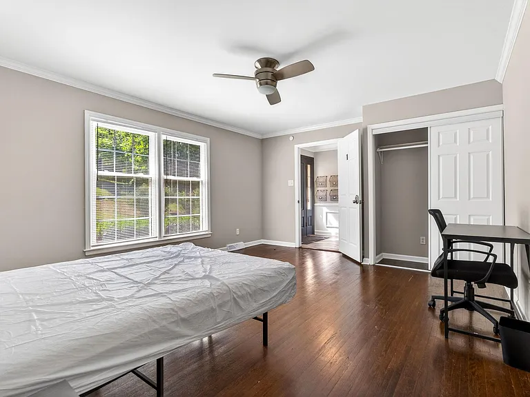 Spacious bedroom with hardwood floors, large windows, ceiling fan, and a wide closet plus a work desk area.