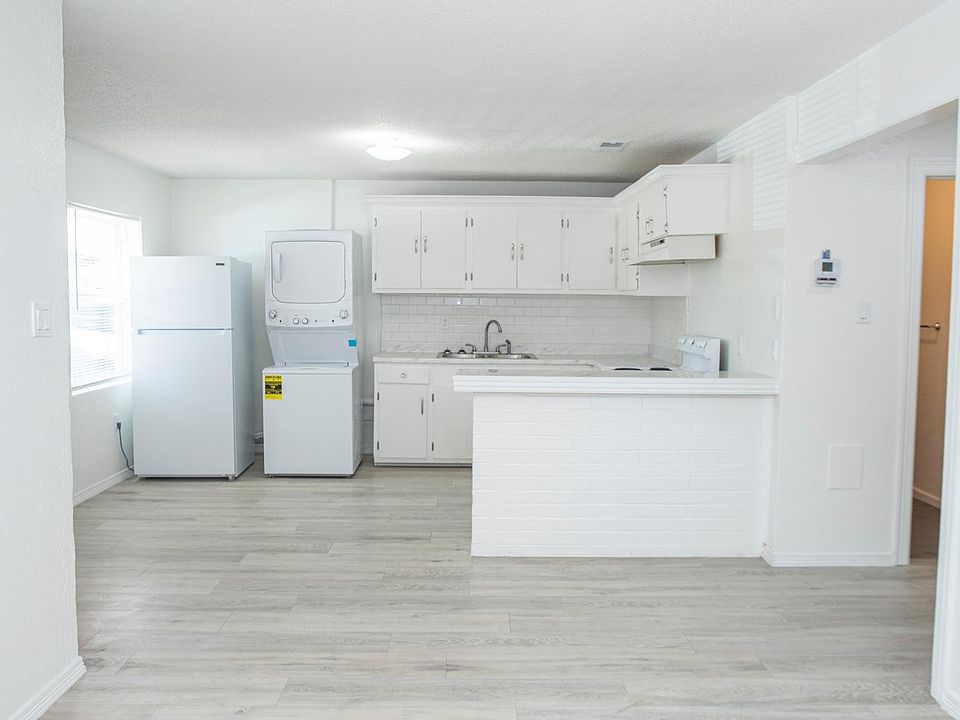Bright kitchen featuring modern white cabinetry, an island with seating space, appliances including a refrigerator and stove. Open layout seamlessly connects to the living area, perfect for entertaining or small family gatherings.