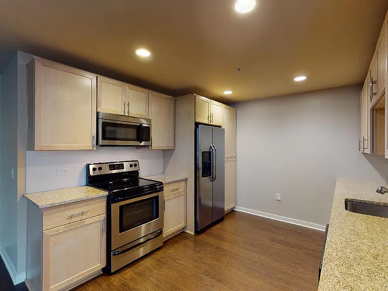 Apartment kitchen with stainless steel appliances, granite countertops and wood-style flooring.