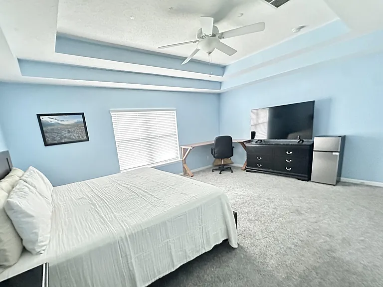 Spacious bedroom with tray ceiling and ceiling fan, plus a work desk, dresser, and mini fridge for added convenience.