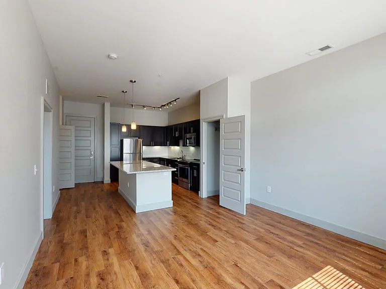 Apartment kitchen with stainless steel appliances, dining and living room with wood-style flooring.