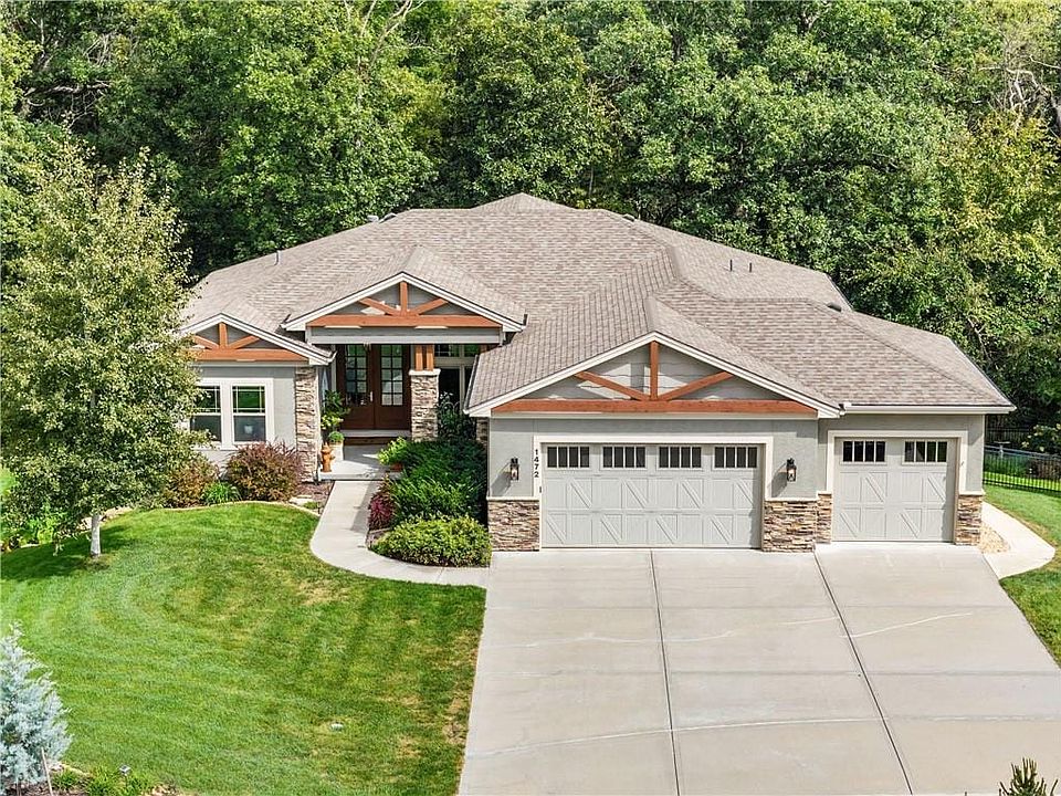 Mature trees frame a modern facade featuring stone accents and a wide concrete driveway.