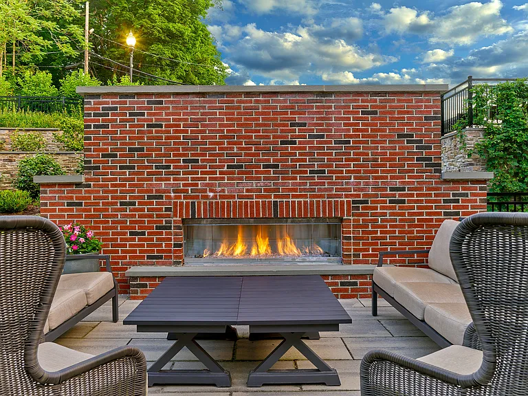 Chic outdoor patio with cozy seating, modern brick fireplace, and lush green surroundings.