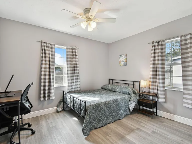 Full size cozy bed, with end table, light, office desk, chair and light as well as storage container under the bed.