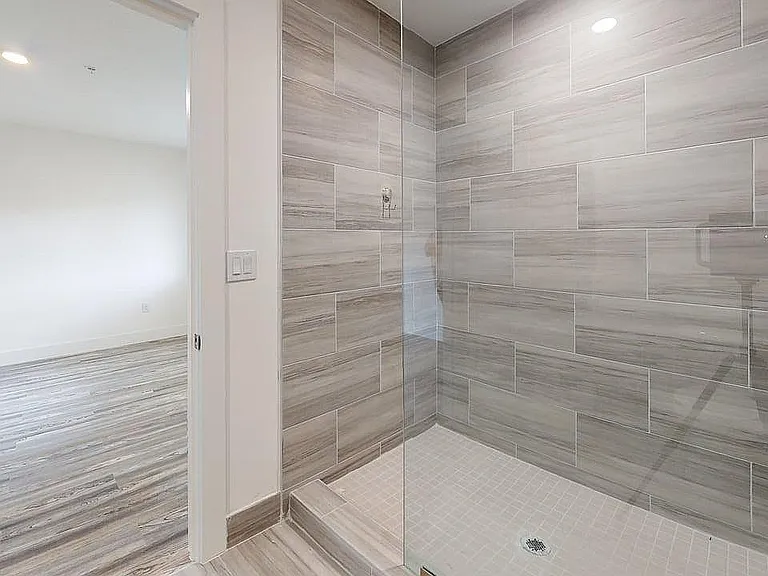 Elegant bathroom featuring a modern glass shower with stylish gray tiles, opening to a bright room with sleek hardwood flooring.