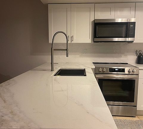 Newly renovated kitchen: white shaker cabinets, marble counter tops, stainless steel appliances with convection oven, microwave, side-by-side refrigerator with ice and water dispenser, and dishwasher.
