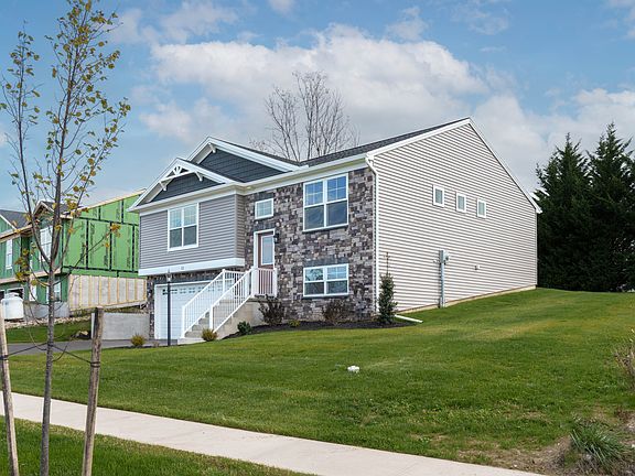 Front angled view of a two-story home with gray siding, stone accents, and red front door on a slope