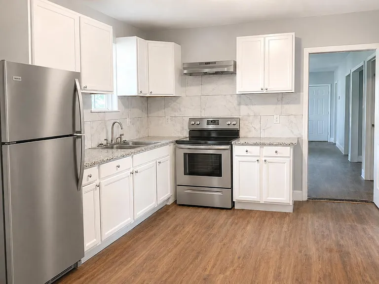 Updated kitchen with white cabinetry, stone-look counters, tile backsplash, and stainless steel range and refrigerator.
