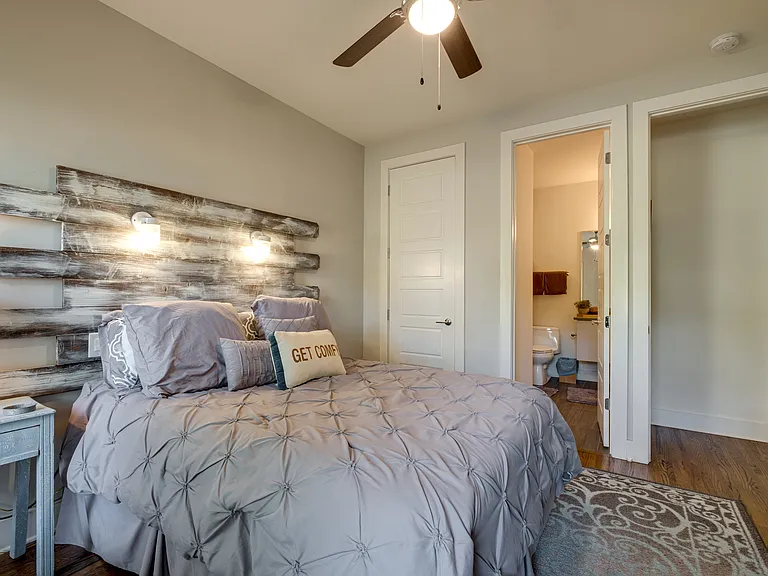 First-floor bedroom with Queen Pillow top bed, featuring a handcrafted custom headboard with mason jar lighting, Roku TV, top-down/bottom-up blackout shades, a walk-in closet, dresser, and direct access to the private ensuite full bathroom.