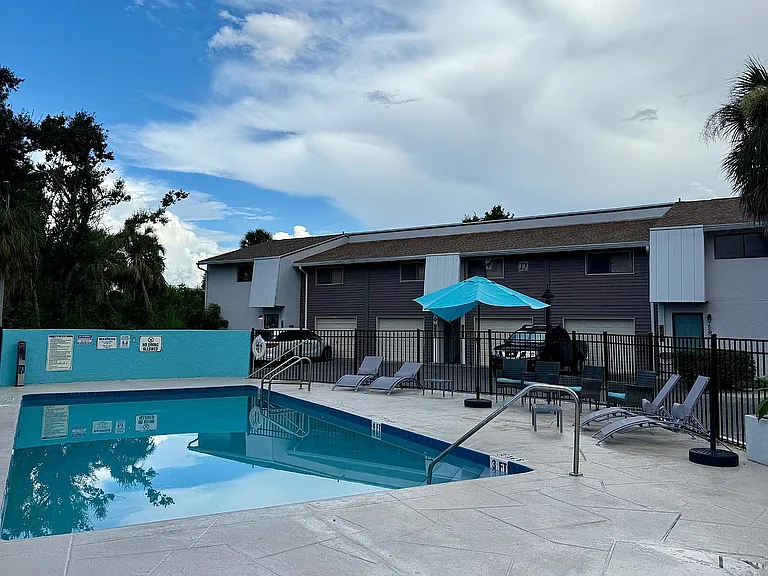 Inviting apartment complex featuring a sparkling outdoor pool, surrounded by elegant lounge chairs and vibrant umbrellas, set against a backdrop of lush greenery.