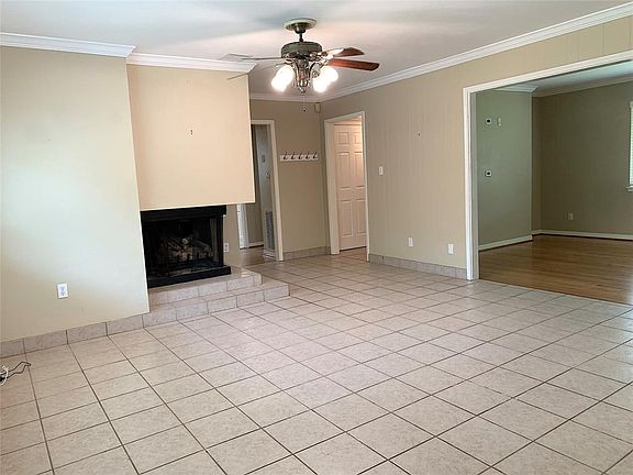 Fireplace with gas logs in family room. Tiled flooring. Ceiling fan and crown molding. Neutral colors.