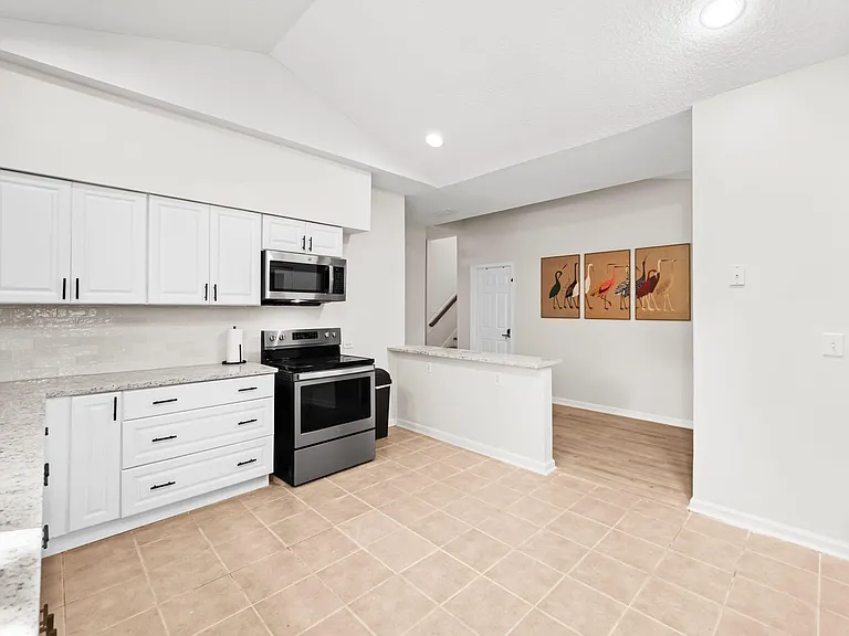 Updated kitchen with white cabinetry, granite-look counters, and stainless range/microwave plus a convenient breakfast bar.
