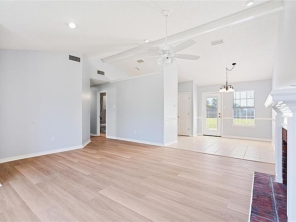 Unfurnished living room featuring ceiling fan with notable chandelier, light hardwood / wood-style floors, and lofted ceiling