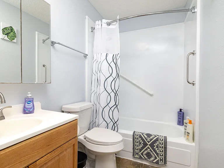 Full bathroom featuring a tub-shower combo, oak vanity, and helpful safety grab bars.