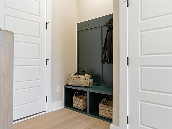 A small entryway with white doors, a green built-in storage unit, and various baskets and bags on th
