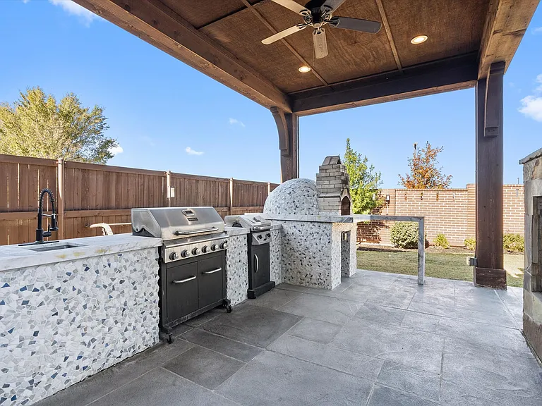The covered pergola facing the pool features a stunning outdoor kitchen and an outstanding decorative stone see-through fireplace!