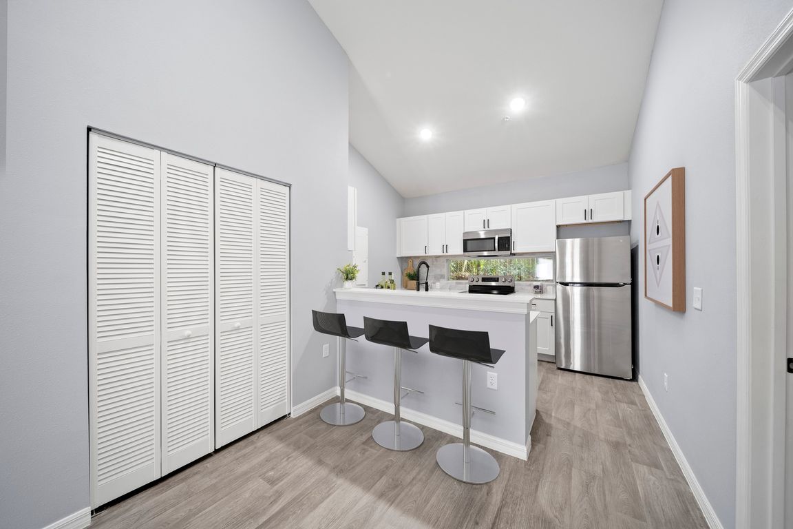 Kitchen with appliances, white cabinets, bar counter and bar height stools