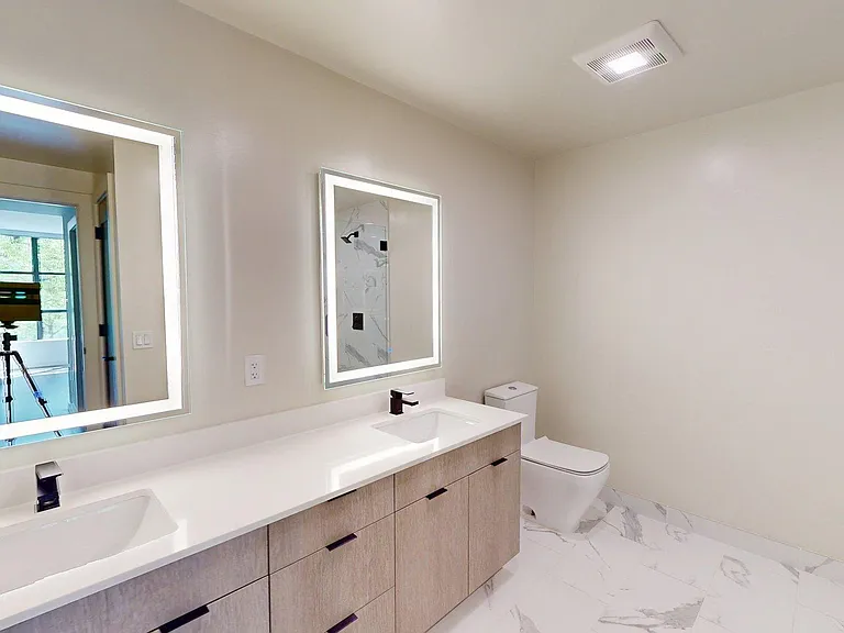 Apartment bathroom with glass-enclosed shower, tile flooring, double sinks, and LED vanity mirror.