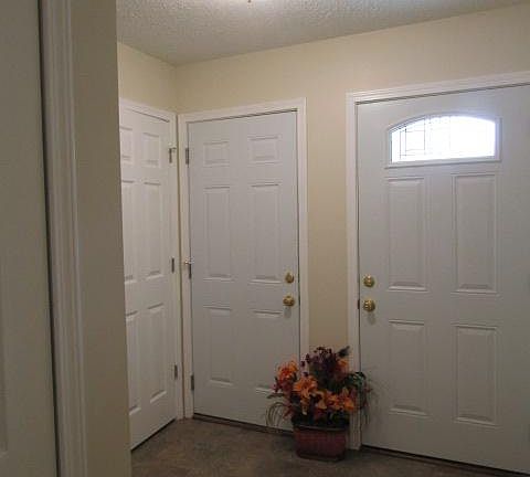 Foyer has (right to left) main entry, garage door, and entry closet. Enclosed light. Cream walls and white trim. Floor is dark gray/brown vinyl tile.