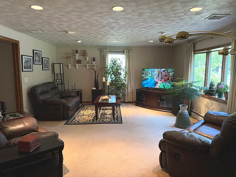 Spacious furnished living room with reclining leather seating and large TV