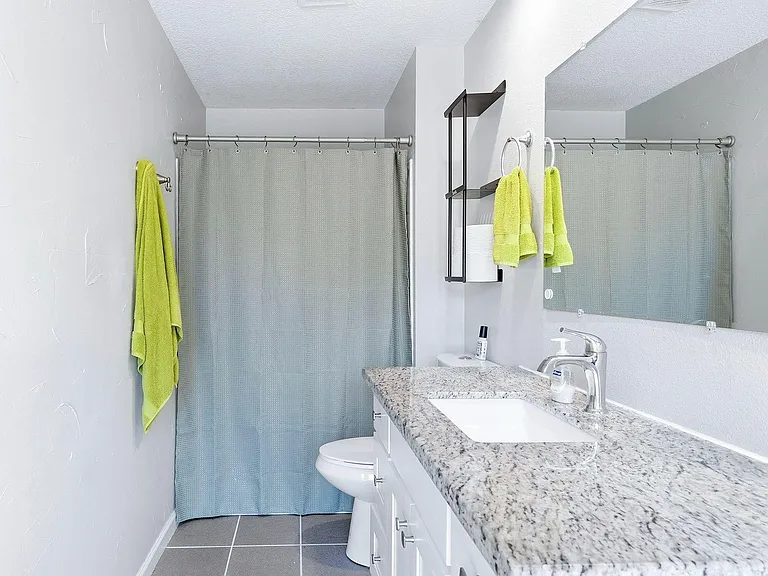 Full bathroom with shower/tub combo, granite-look vanity, large mirror, and under-sink storage for daily essentials.
