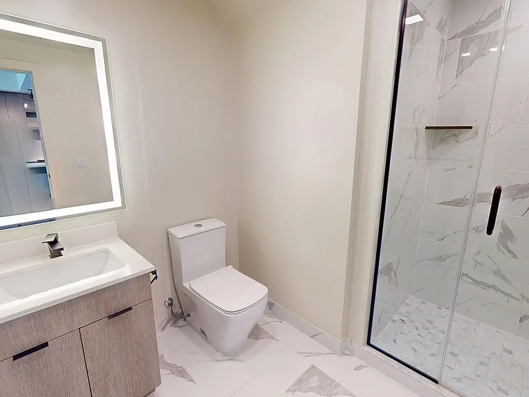 Apartment bathroom with glass wall shower and LED lighted mirror.