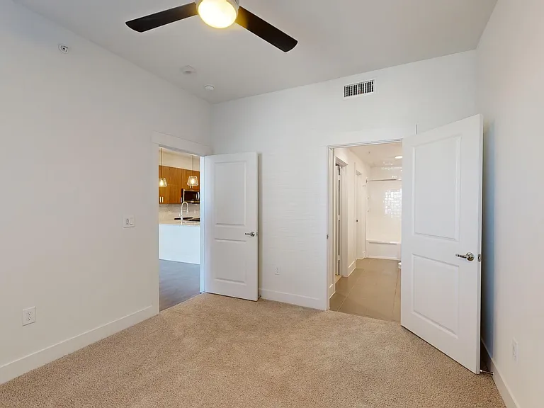 Spacious apartment bedroom with large closet, attached bathroom, and plush carpet flooring.