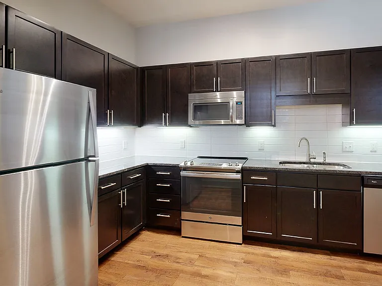 Apartment kitchen with stainless steel appliances, granite countertops and wood-style flooring.