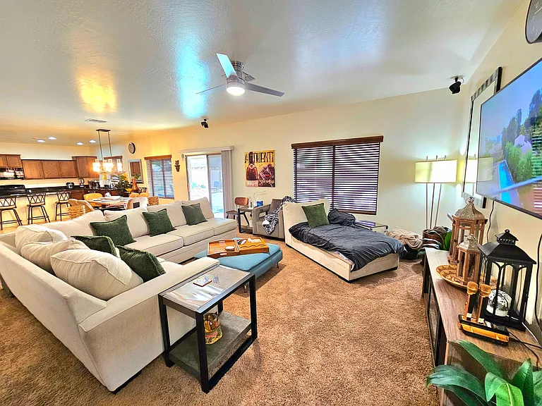 Open-concept living area with sectional seating, ceiling fan, and easy flow to the dining space and kitchen with bar seating.