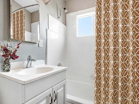 Bathroom with single vanity, tub and shower combo with white wall tiles