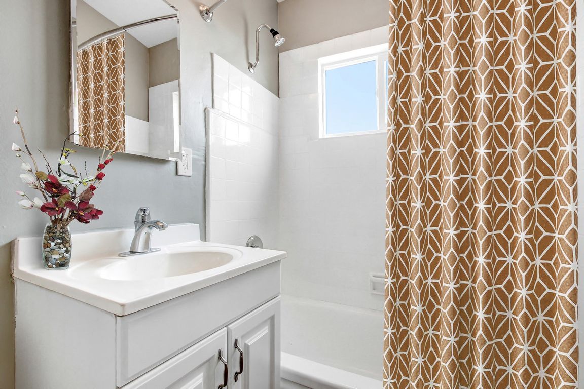 Bathroom with single vanity, tub and shower combo with white wall tiles