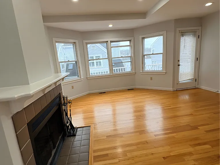 Spacious living area with hardwood floors, large windows, and a cozy fireplace.