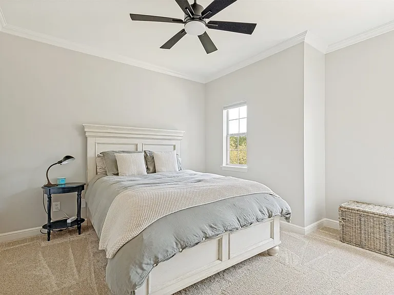 Spacious room featuring vaulted ceilings, crown molding, a ceiling fan with light fixture, two windows providing natural illumination, and plush carpet flooring