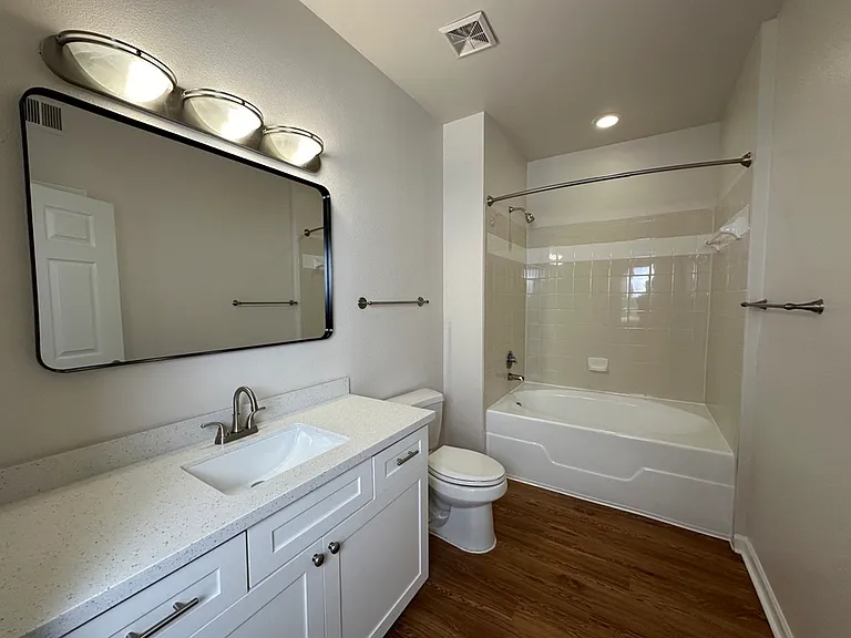 Modern bathroom featuring a sleek vanity with a large mirror, elegant lighting, quartz countertop, and a pristine bathtub with tiled walls. Modern bathroom featuring a sleek vanity with a large mirror, elegant lighting, quartz countertop, and a pristine b