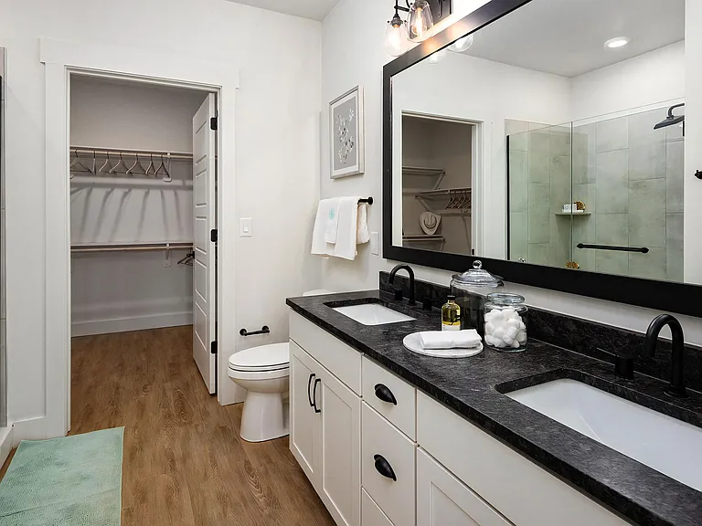 En-suite bath featuring walk-in glass shower, white cabinets, toilet, and doorway to spacious closet