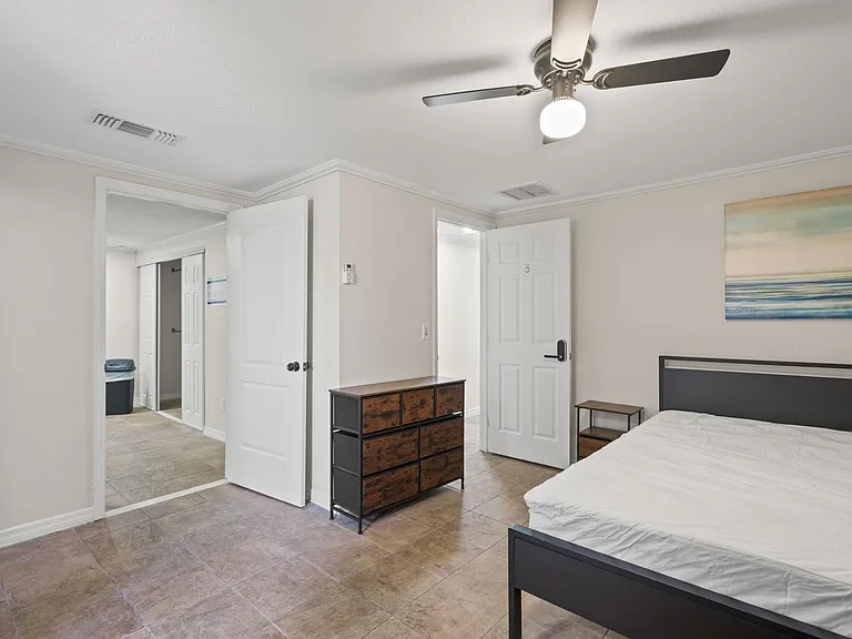 Spacious bedroom with tile flooring, ceiling fan, and furnished setup including bed, dresser, and nightstand.