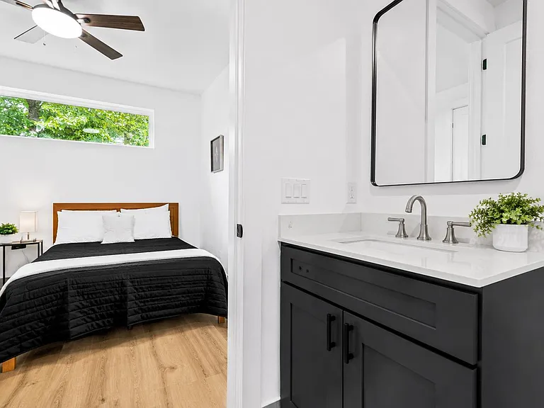 Bedroom with a ceiling fan, high window, and adjacent vanity area with quartz-style counter and ample storage.