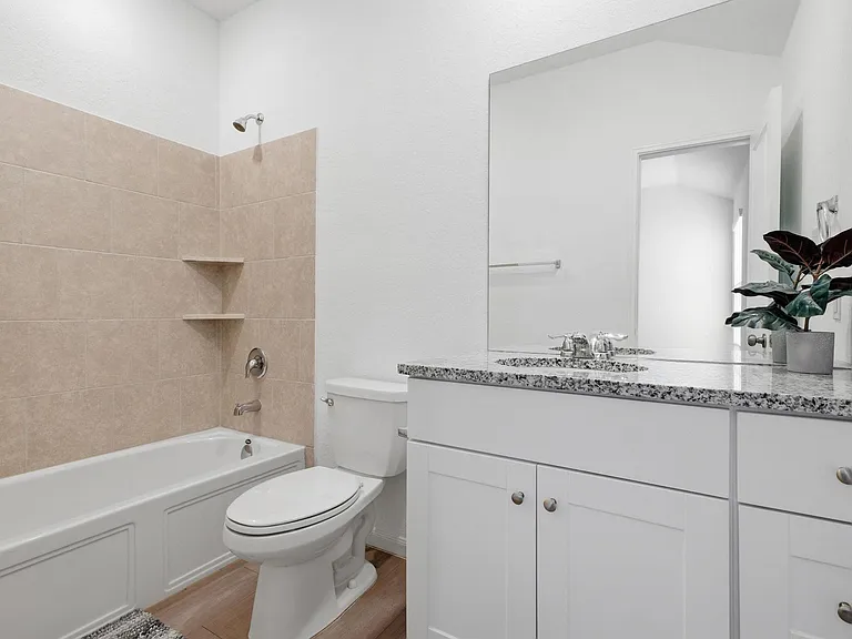 Full bath with tiled tub/shower, spacious granite-top vanity, and ample cabinet storage for daily essentials.