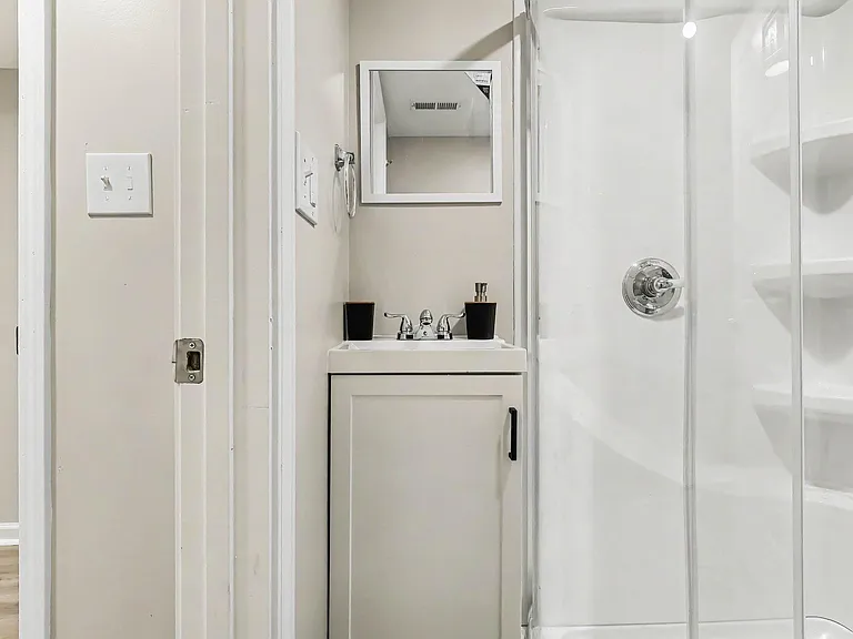 Compact bathroom with a single-sink vanity, mirrored medicine cabinet, and walk-in shower with built-in shelving.