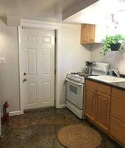 Kitchenette with stove, sink and garbage disposal, refrigerator, cabinets and open shelving for storage.
