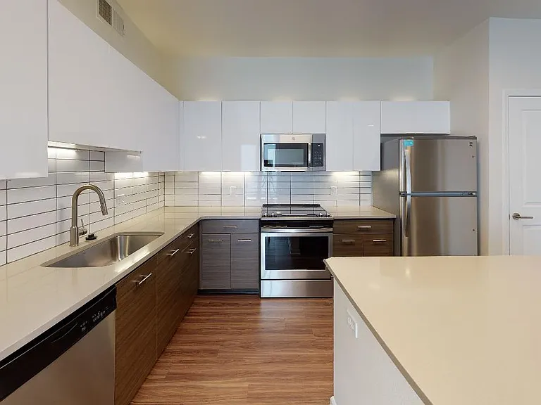 Apartment kitchen with stainless steel appliances, quartz countertops and wood-style flooring.