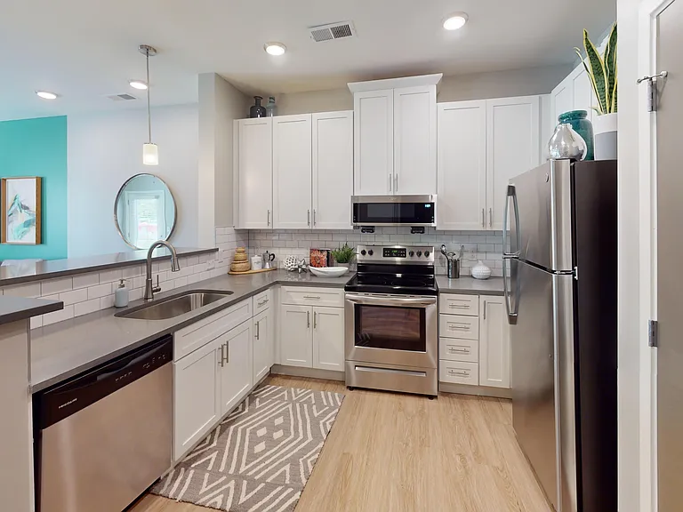 White cabinetry, stainless steel appliances, and pendant lighting meet in this open-concept kitchen that flows seamlessly into your living space.