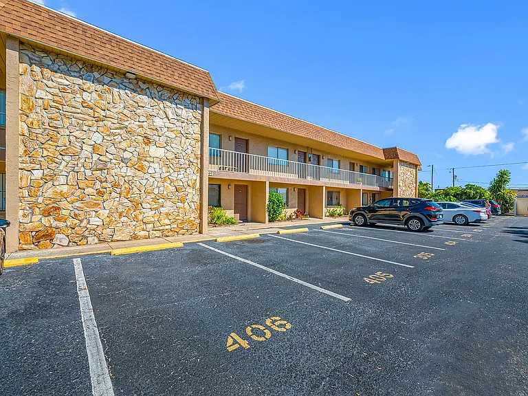 Inviting two-story apartment complex with stone facade, ample parking, and lush greenery under a clear blue sky.