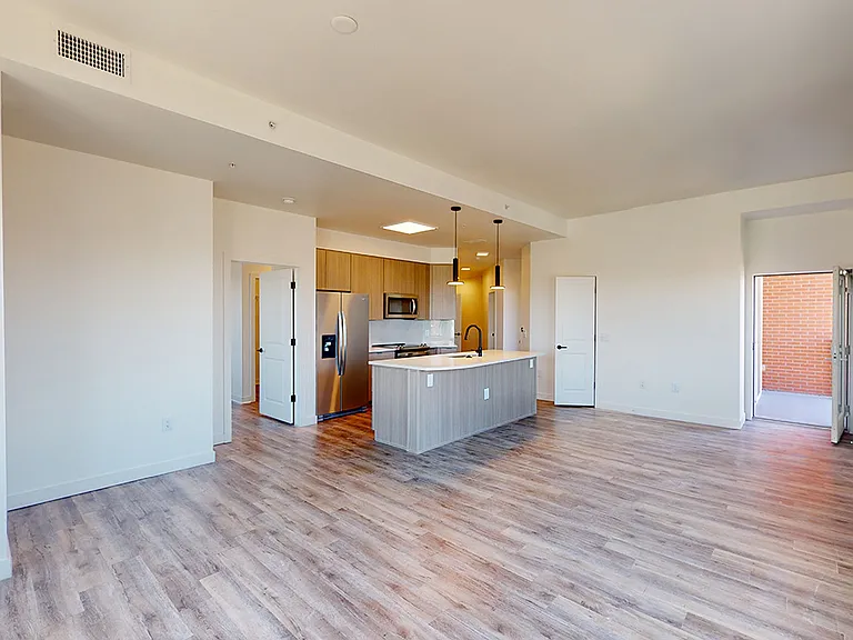 Apartment kitchen with stainless steel appliances, dining and living room with wood-style flooring.