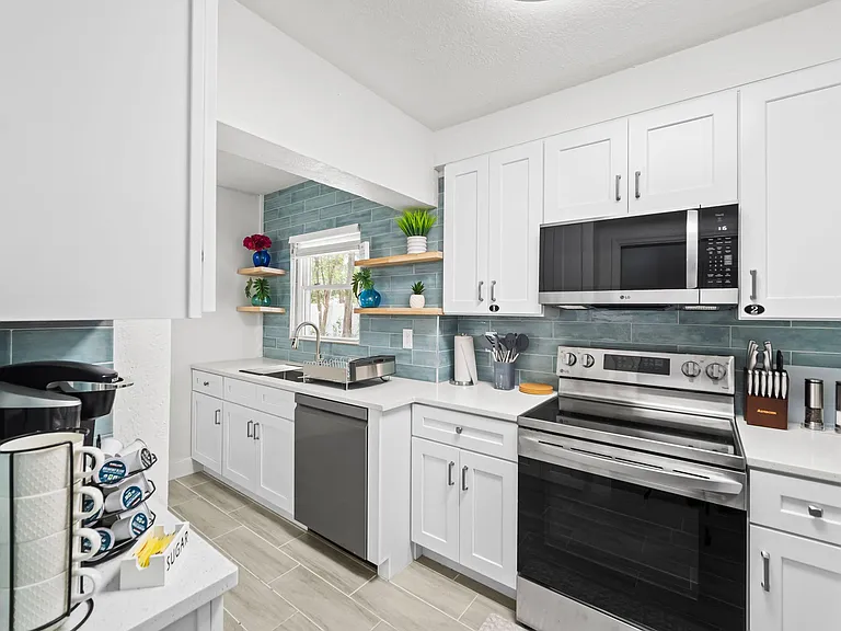 Updated kitchen with stainless steel range and microwave, ample white cabinetry, open shelving, and a window over the sink.
