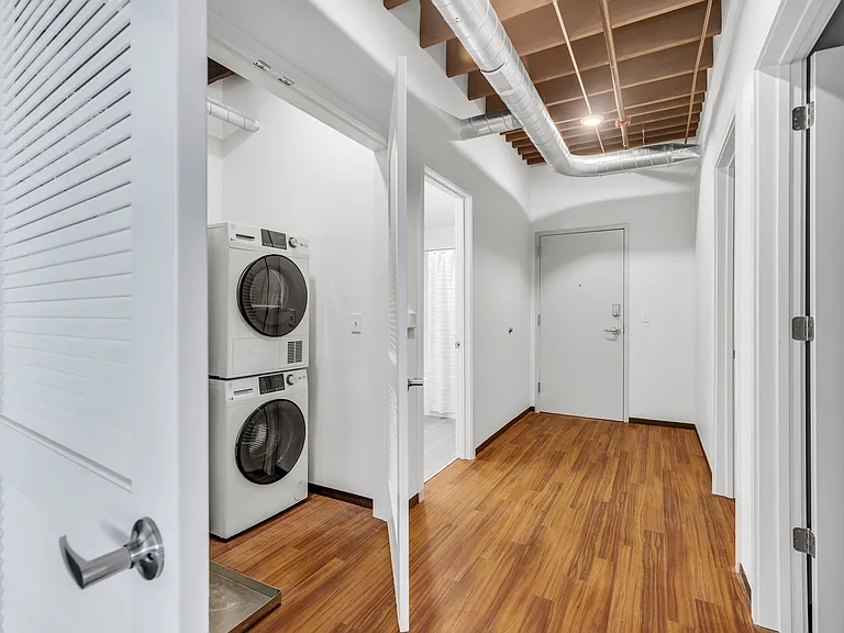Laundry Convenience: An organized entry hall highlighting a neatly tucked-away laundry room, with white appliances and louvered doors, set against warm wooden flooring.