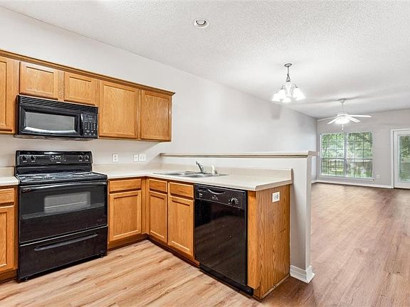 Kitchen with ceiling fan with notable chandelier, light hardwood / wood-style floors, black appliances, decorative light fixtures, and sink
